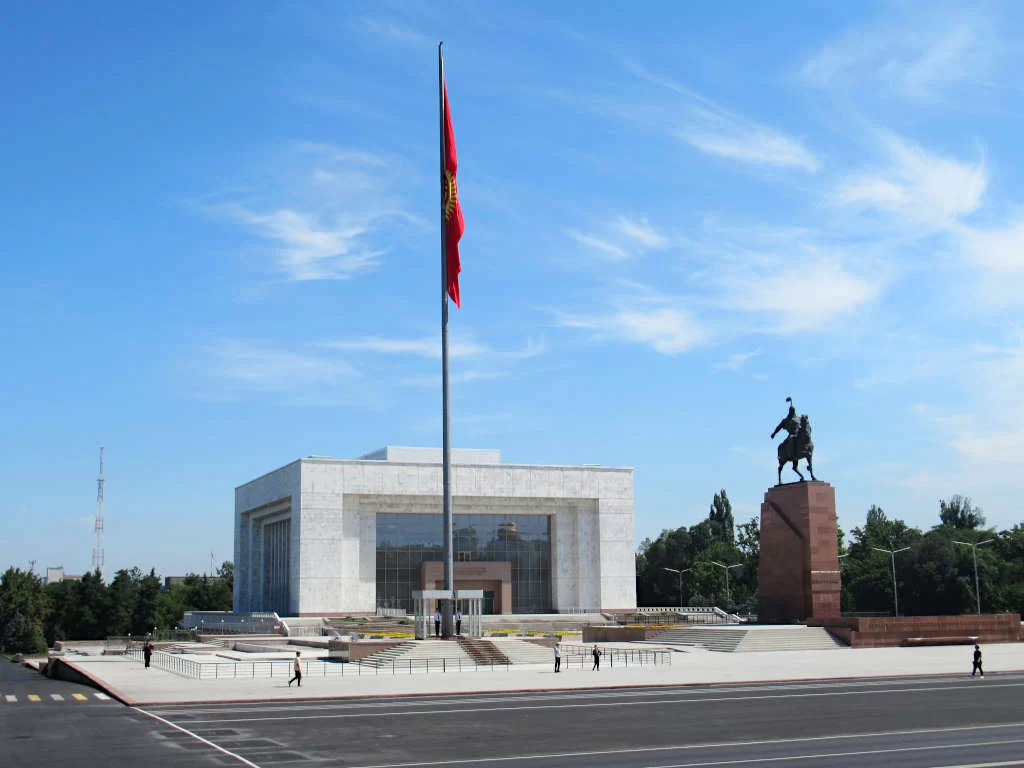 The history museum, a statue and a large flag of Kyrgyzstan make up the square under a blue sky