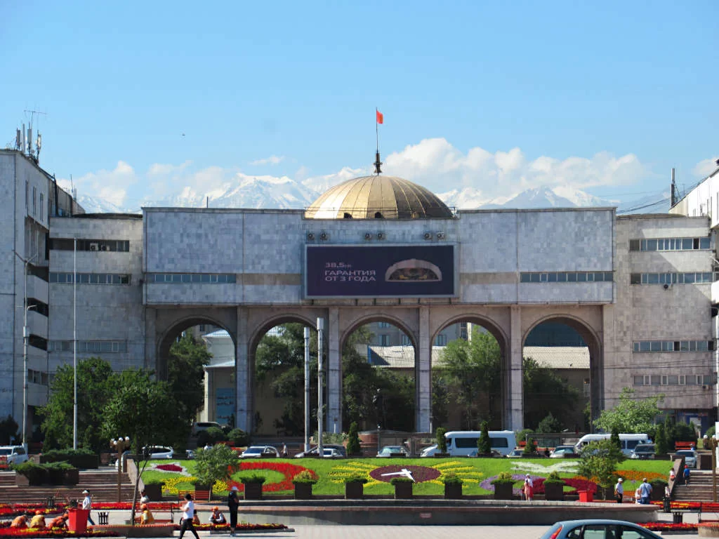 The snowy mountains of Kyrgyzstan behind the golden dome-topped building in Ala Too Square