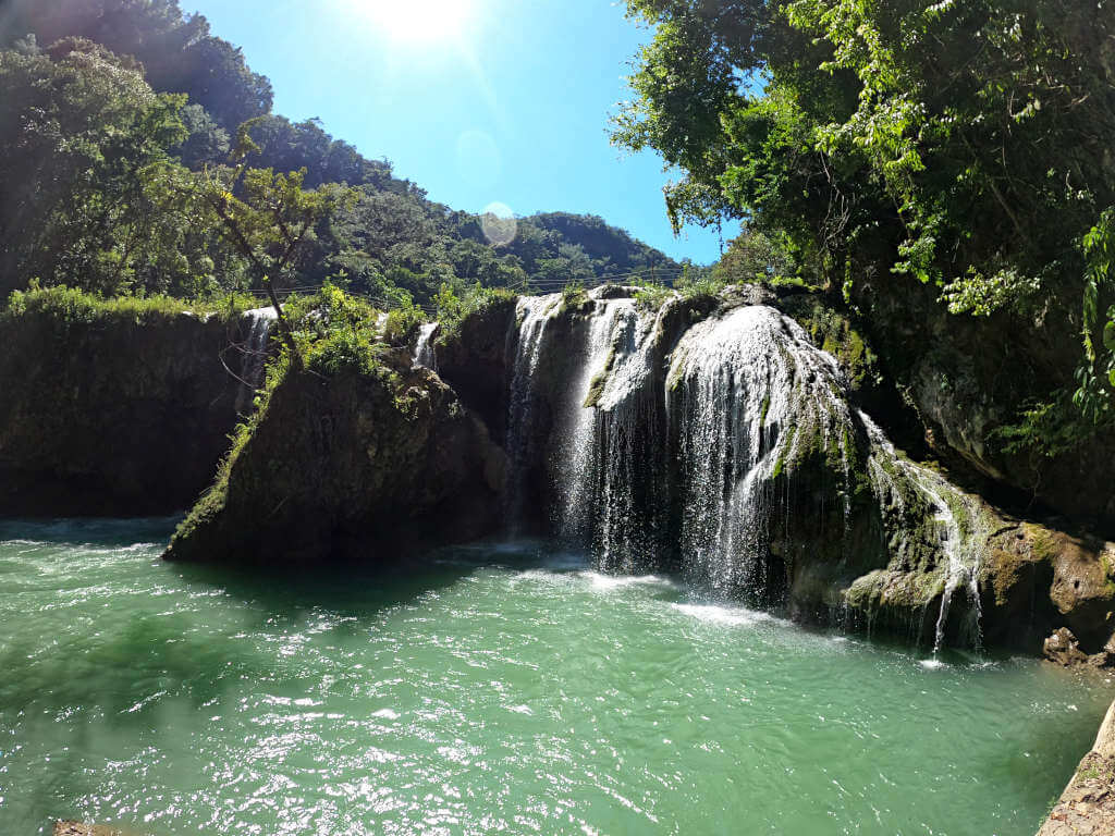 A waterfall along the river surrounded by green trees and under a blue sky