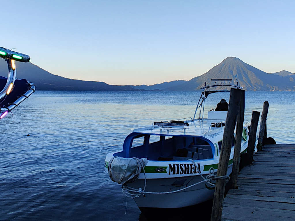 A lancha boat on Lake Atitlan at the dock with the large and imposing volcano behind. This is an important part of the journey from some of the Lake Atitlan towns to Semuc Champey