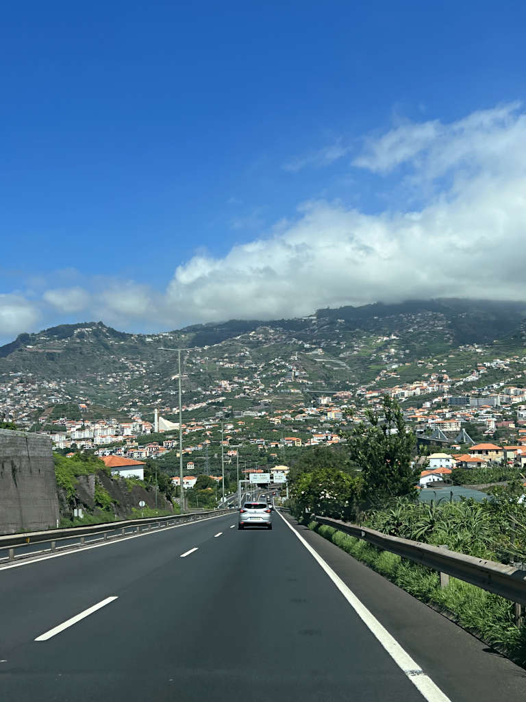 Driving is the easiest way to get around in Madeira and car hire is inexpensive. Pictured from the passenger seat is the main highway as it approaches Funchal with houses scattered on the hillside