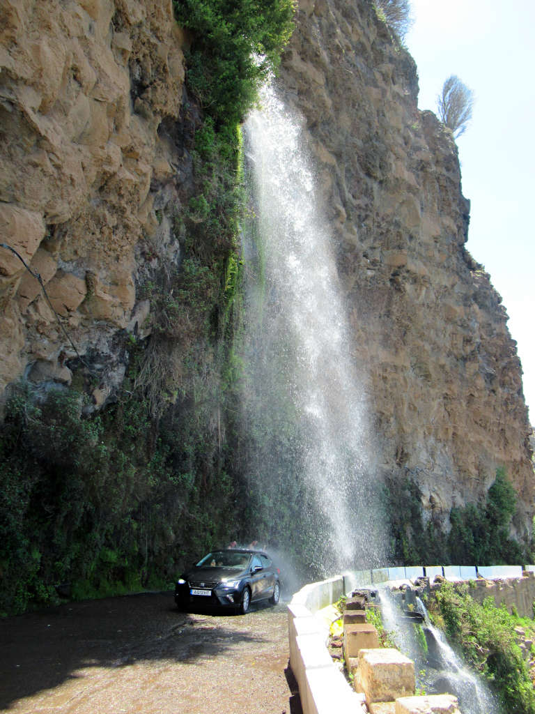 The Cascata Dos Ajos Waterfall falls over the road and here a car drives underneath.