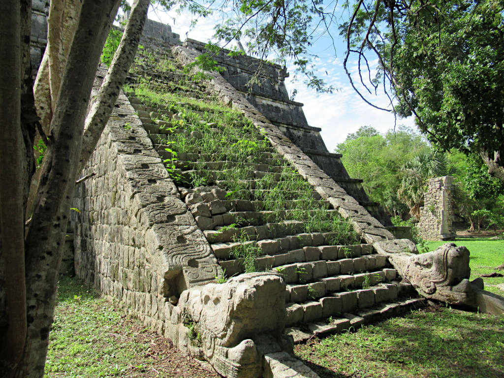 A smaller temple at Chichen Itza that is less restored and has grass growing through the temple steps