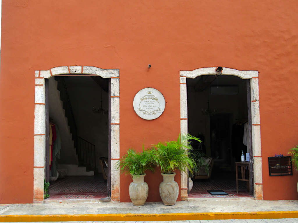 An orange building in Valladolid with two doors and two plants outside