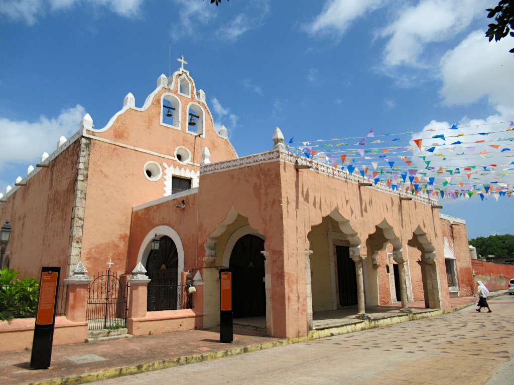 A nun walking into a church in Valladolid under the cover of colourful bunting and blue sky