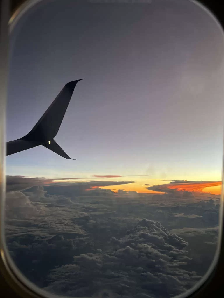 Looking out an airplane window as the sunsets in the distance behind the clouds