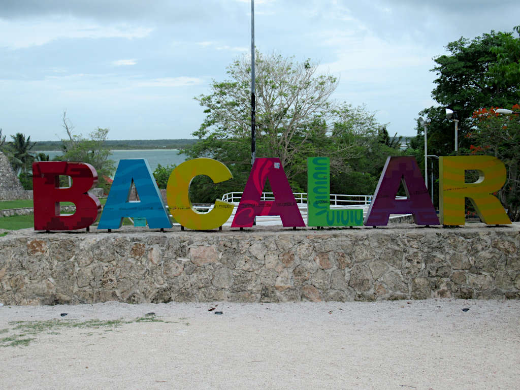 Large letters in different colours that spell out Bacalar with the lagoon behind