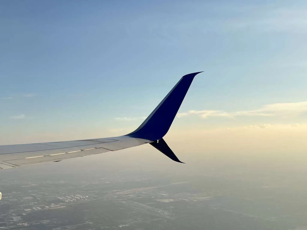 Looking out the right-hand side of a plane with the wing tip visible and a hazy sky below. Flying is one way to get from Cancun to Caye Caulker