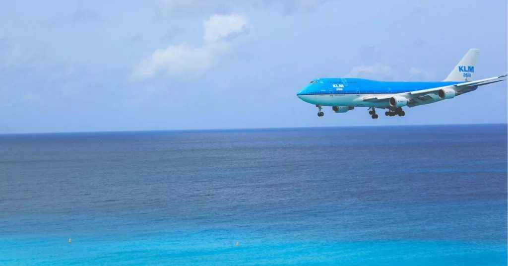A blue KLM plane coming in to land over a bright blue sea