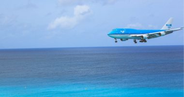 A blue KLM plane coming in to land over a bright blue sea