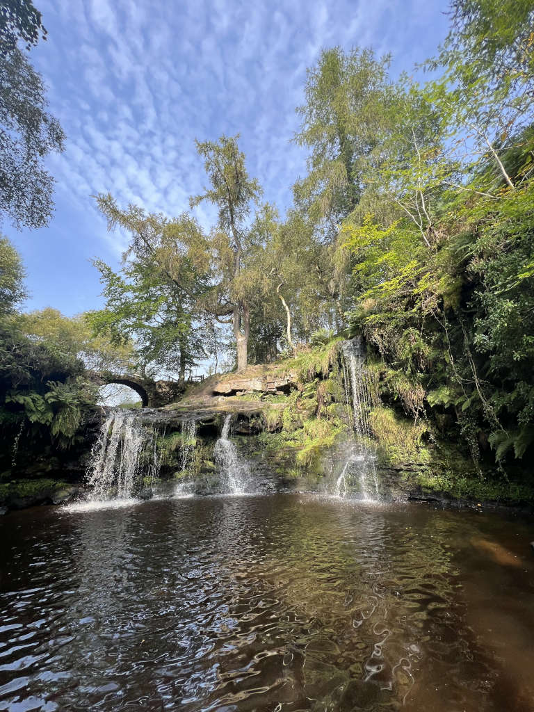 The view of the waterfall from the bottom looking up at the water and bridge behind