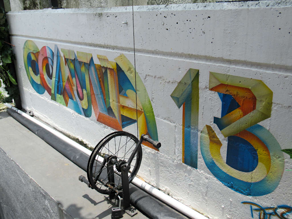 The words Comuna 13 are painted on white wall in bright colours