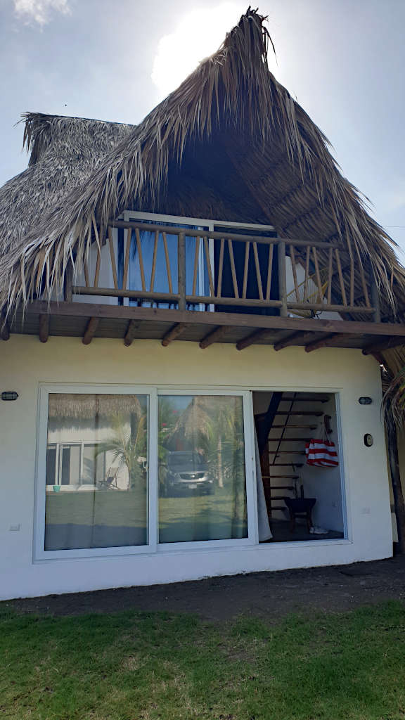A cabana on the pacific coast with a thatched room and two floors.
