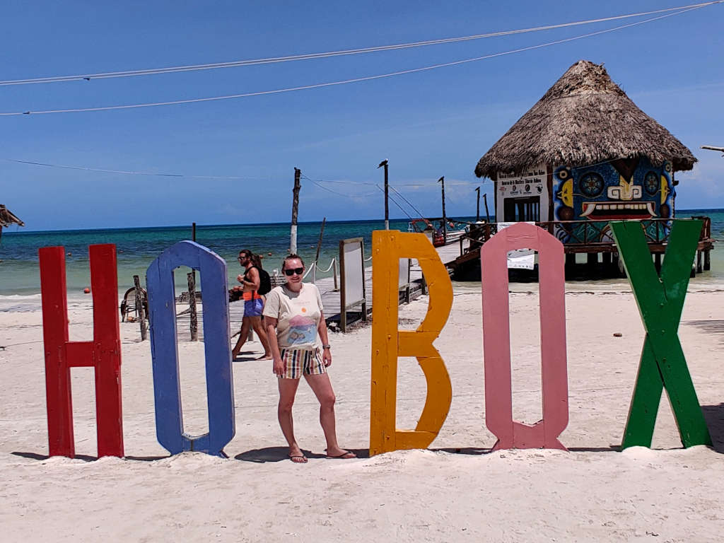Zoe stood as the L in the Holbox sign with a thatched top building behind her