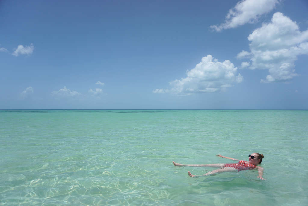 Once you complete the journey from Merida to Holbox you'll be rewarded with swimming in the warm, calm, clear blue seas, like Zoe is doing here. The sun is out and the sky is blue with just a couple of fluffy white clouds.